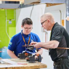 Plumbing student and lecturer placing metal pipe into clamp